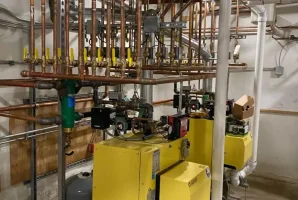 Industrial boiler room with yellow boilers, complex network of copper pipes, and control valves.