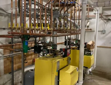Industrial boiler room with yellow boilers, complex network of copper pipes, and control valves.