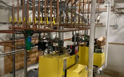 Industrial boiler room with yellow boilers, complex network of copper pipes, and control valves.