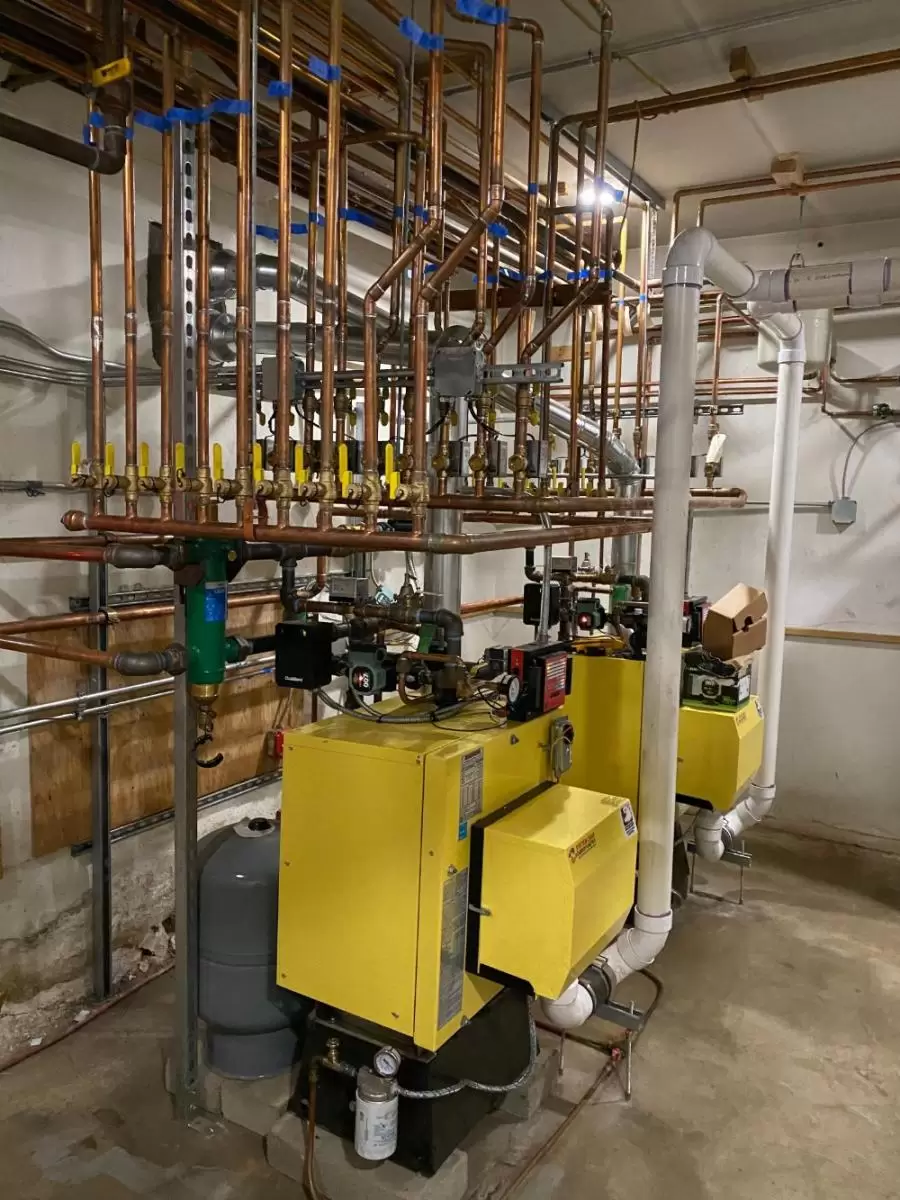 Industrial boiler room with yellow boilers, complex network of copper pipes, and control valves.