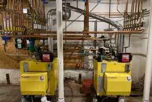 Two yellow boilers with copper piping in a utility room.