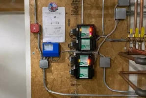 Mechanical control panel with wiring and pipes on a wooden board in a utility room.