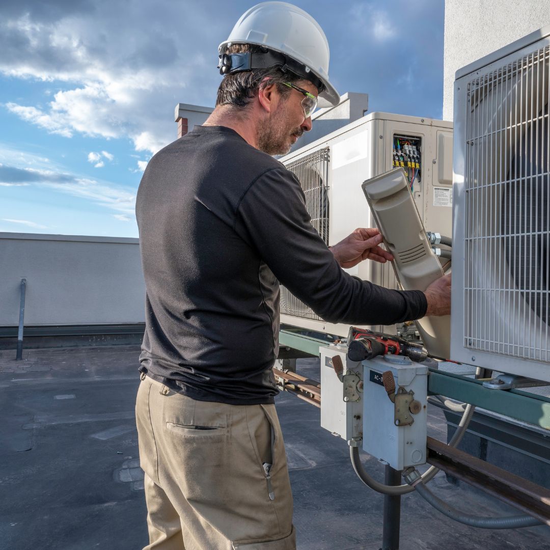 HVAC technician working on a unit on a roof.