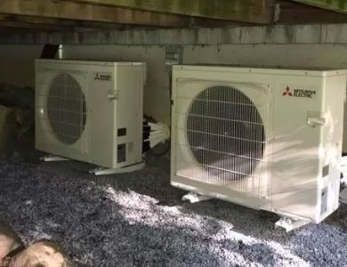 Two Mitsubishi Electric outdoor HVAC units on a gravel surface under a building structure.
