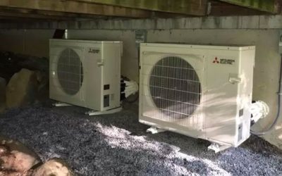 Two Mitsubishi Electric outdoor HVAC units on a gravel surface under a building structure.
