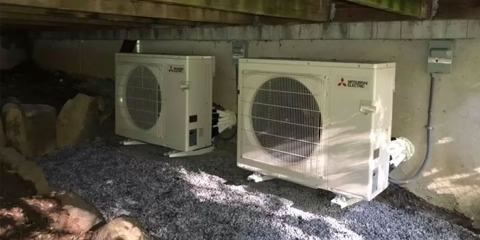 Two Mitsubishi Electric outdoor HVAC units on a gravel surface under a building structure.