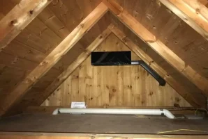 Wooden attic with a triangular roof and an air conditioning unit venting at the top.