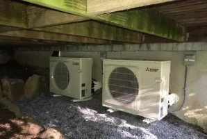 Mitsubishi air conditioning units installed under a wooden deck with gravel ground.