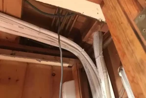 Cables and pipes running through a wooden ceiling space, showcasing building infrastructure.