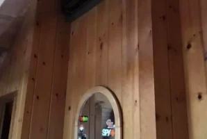 Wood-paneled room with air conditioner above a mirror, displaying various stickers in the reflection.