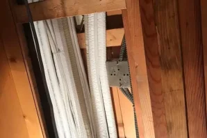 Exposed pipes and cables on a wooden ceiling in construction site.