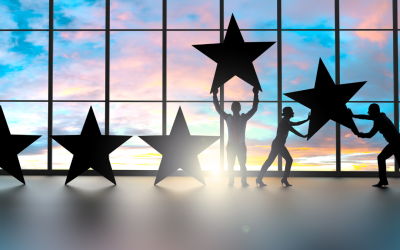 Silhouettes holding large stars in front of a window with a sunset sky.
