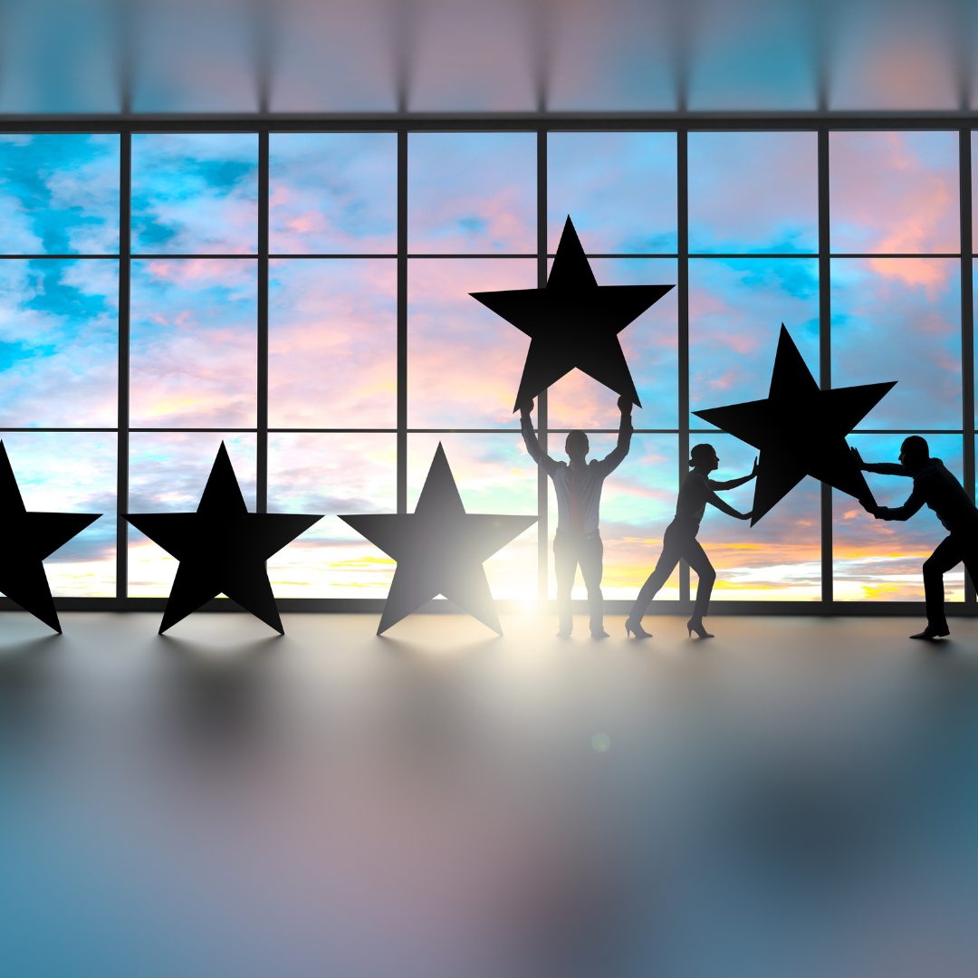 Silhouettes holding large stars in front of a window with a sunset sky.