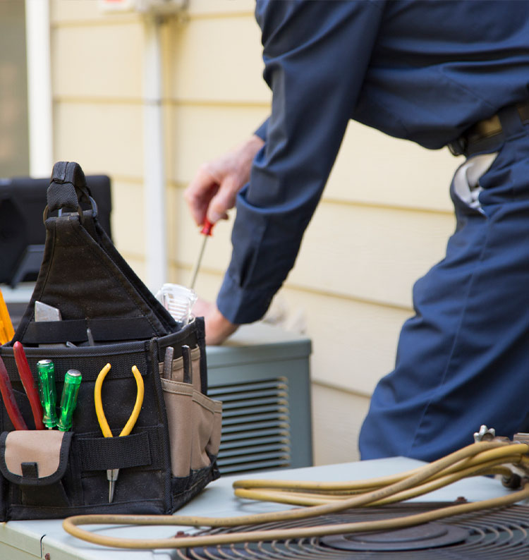 Technician servicing AC unit with tool kit and coiled cables on the side.