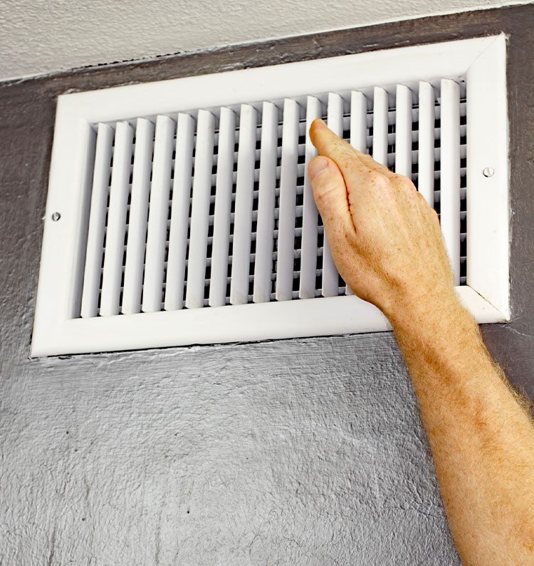 Hand adjusting a white air vent on a gray wall for airflow control.
