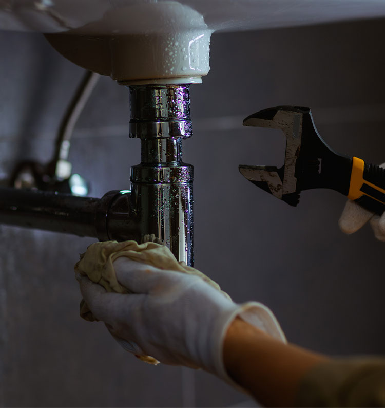 Plumber in gloves fixing sink pipe with wrench and cloth.