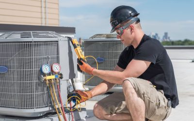 Technician servicing rooftop HVAC unit with gauges and tools.