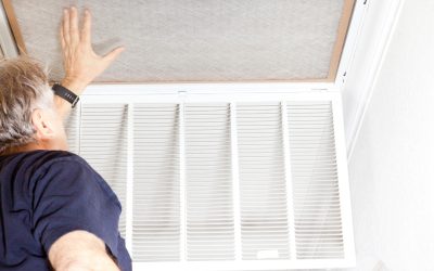 Person replacing an air filter in a ceiling vent for home maintenance.