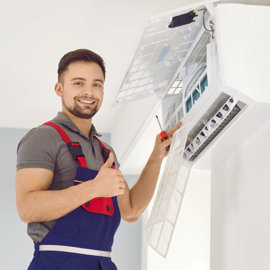 Technician smiling, repairing air conditioning unit with thumbs up.