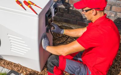 Technician in red uniform working on outdoor electrical generator with tools nearby.
