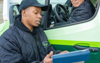 Two men in Clover-branded jackets review a clipboard beside a green van.