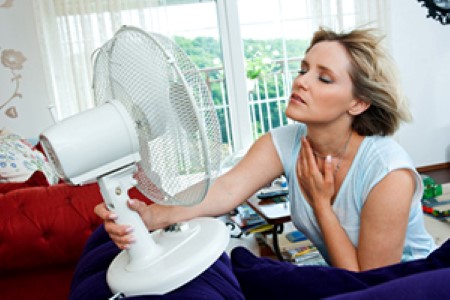 Woman cooling down in front of a fan inside a living room.
