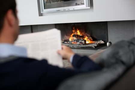 A person reading a newspaper by a cozy fireplace at home.