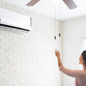 A woman adjusting a remote-controlled air conditioner in a bright room.