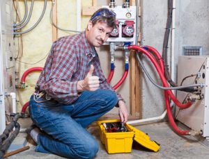 A plumber giving a thumbs up while working on a boiler with tools in a basement.