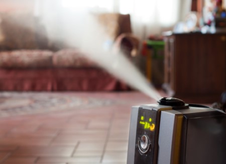 Humidifier releasing mist in a cozy living room with a sofa and soft lighting.