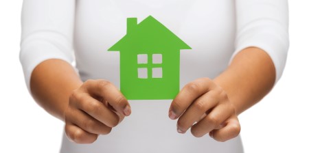 Person holding a green paper house cutout, symbolizing home ownership or sustainable living.