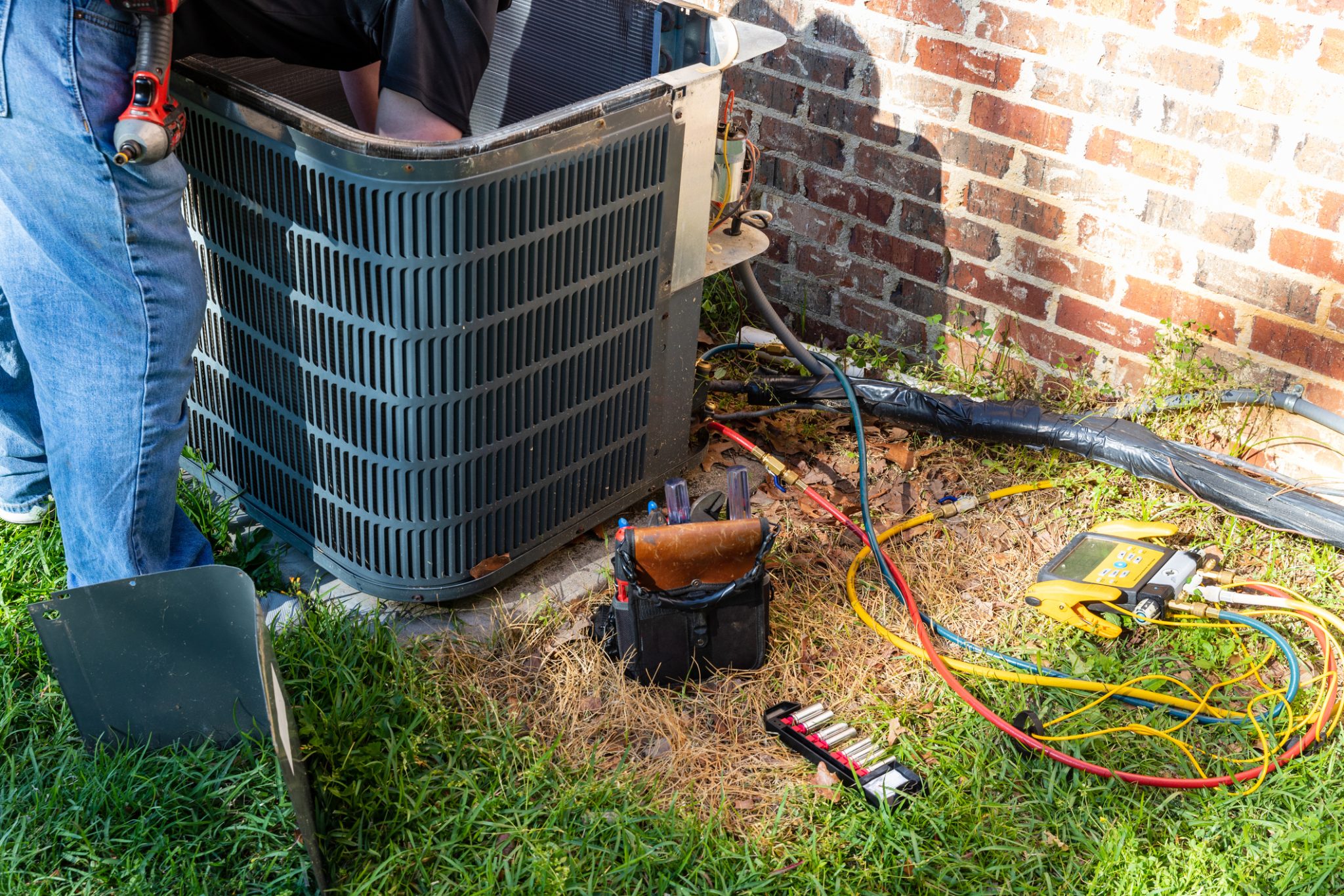 HVAC technician repairing outdoor air conditioning unit with gauges during AC repair and maintenance service