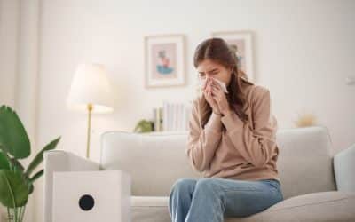 A man sitting at his desk sneezes into a tissue, reacting to allergens and poor indoor air quality.