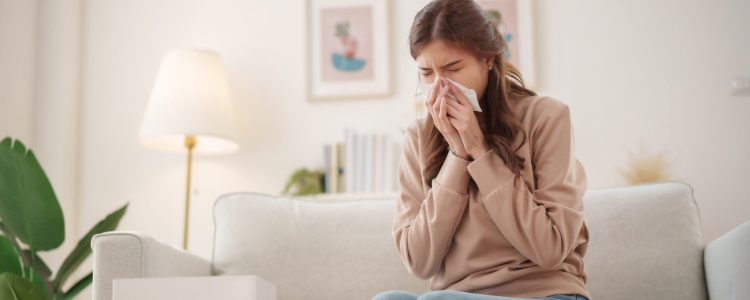 A man sitting at his desk sneezes into a tissue, reacting to allergens and poor indoor air quality.
