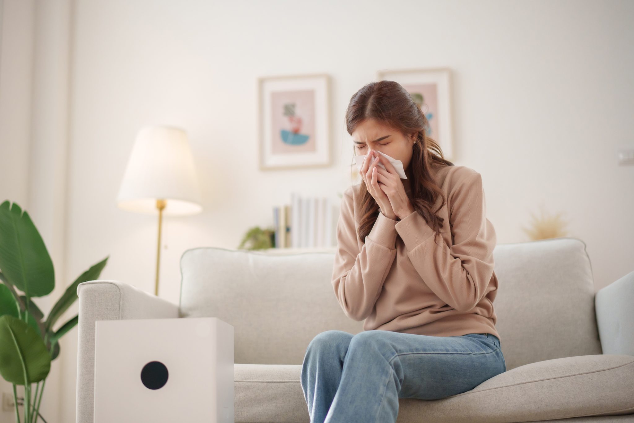 A man sitting at his desk sneezes into a tissue, reacting to allergens and poor indoor air quality.