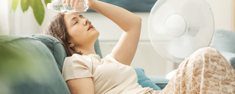 Young woman sitting on the couch at home, suffering from the heat and a poorly maintained AC.