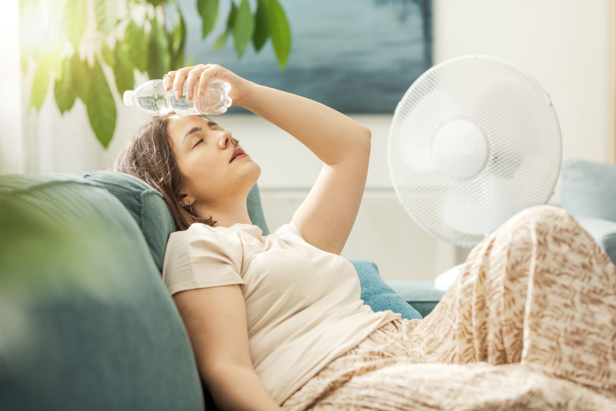 Young woman sitting on the couch at home, suffering from the heat and a poorly maintained AC.