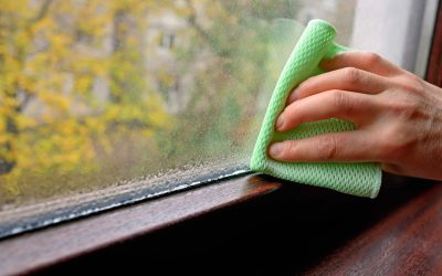 Homeowner wiping condensation from a window interior, a common sign of high indoor humidity in summer.