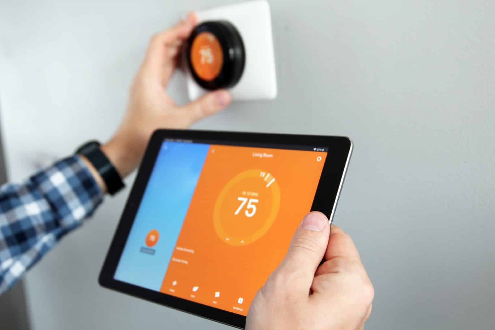 A homeowner adjusting a smart thermostat with a tablet app showing the temperature and schedule controls.