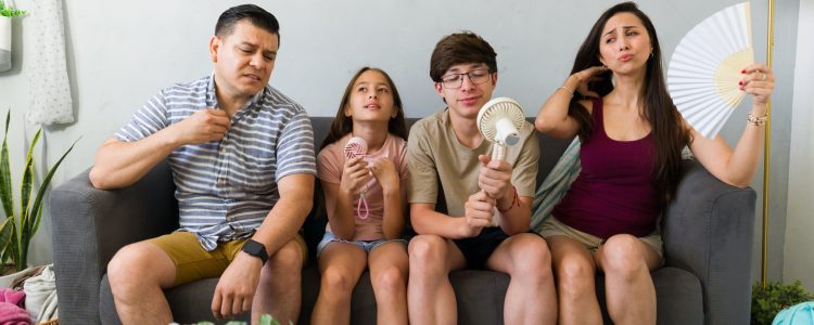 Uncomfortable family uses fans indoors during a summer heat wave, needing AC repair or cooling tips.